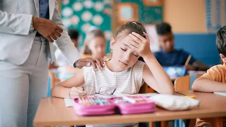 Kind sitzt im Klassenzimmer mit Kopfschmerzen