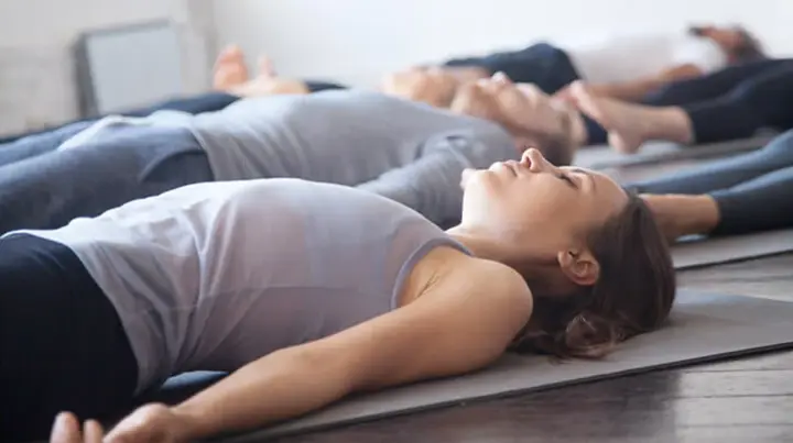 Mehrere Patientinnen und Patienten liegen auf einer Yogamatte und entspannen sich. 