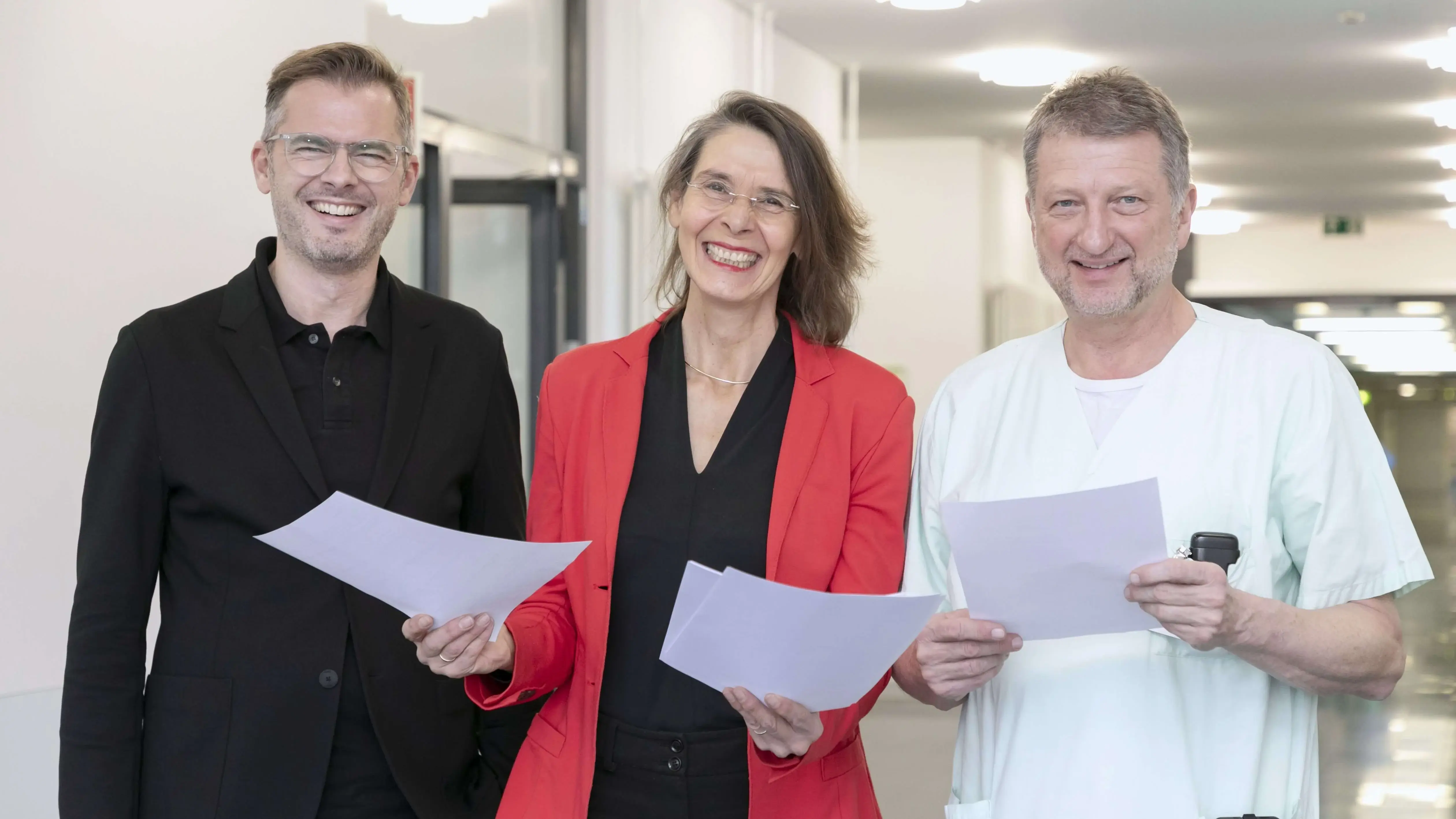 Dr. Ronny Jung, Dr. Susanne Simen und Prof. Dr. Christoph Fusch stehen gemeinsam lächelnd im Flur .