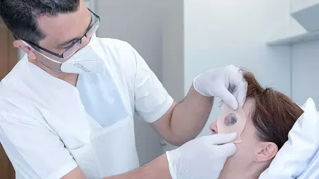 Nach dem Eingriff legt ein Mitarbeitender einer Patientin einen Okklusionsverband am Auge an.