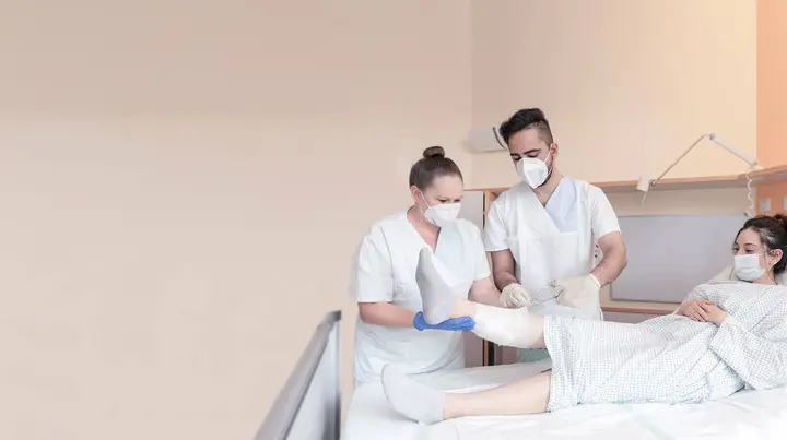 Zwei Mitarbeitende kümmern sich um das Bein einer Patientin. 