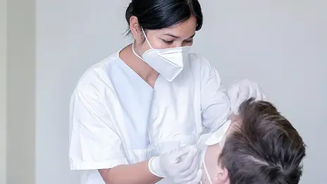 Eine Mitarbeiterin der Augenheilkunde legt einem Patienten einen Augenverband an. 