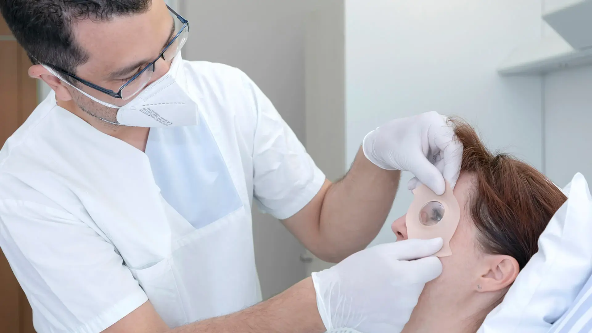 Nach dem Eingriff legt ein Mitarbeitender einer Patientin einen Okklusionsverband am Auge an.