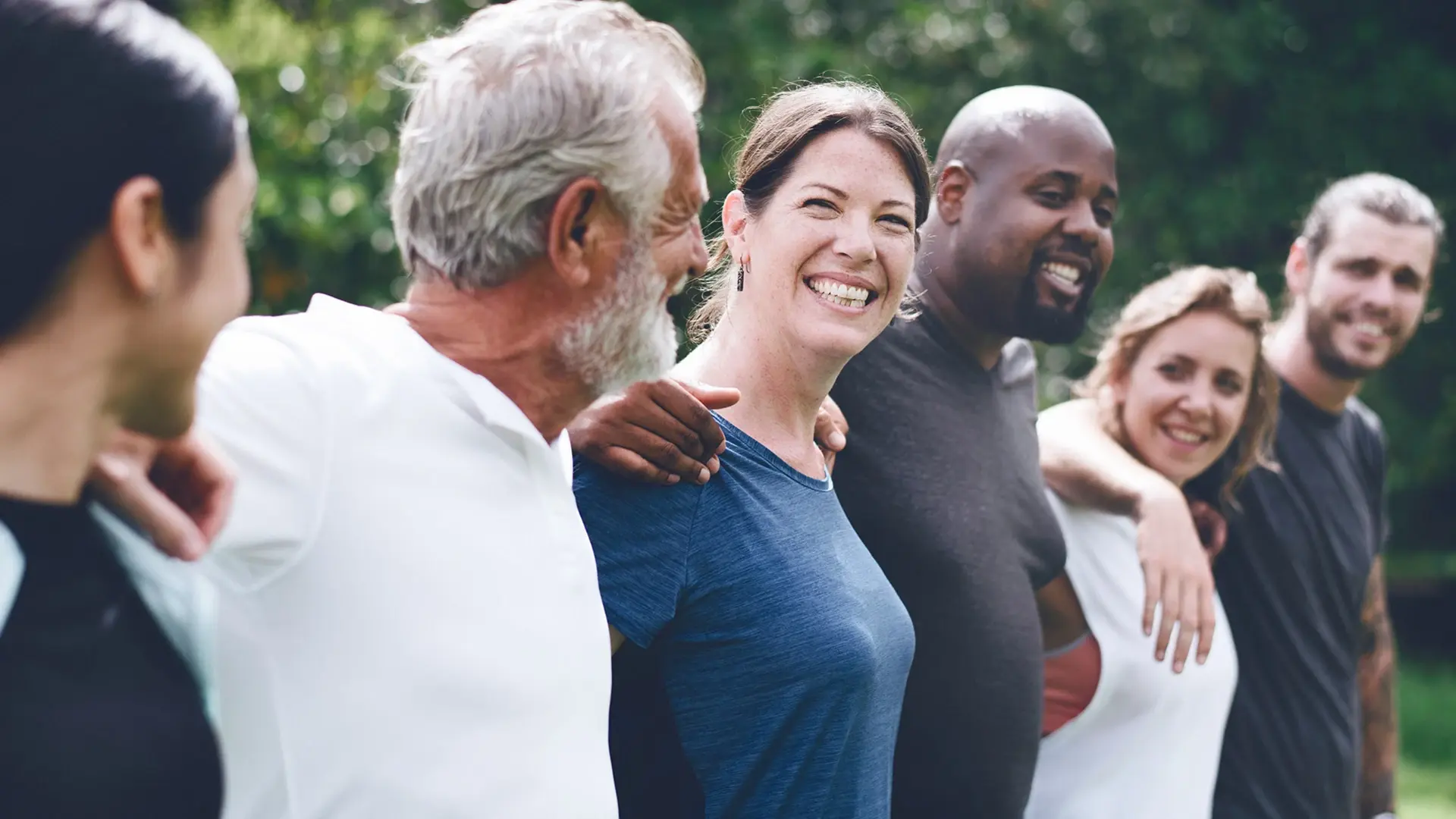 Mehrere Menschen stehen im Rahmen einer Gruppentherapie zusammen. Sie lachen sich gegenseitig an. 