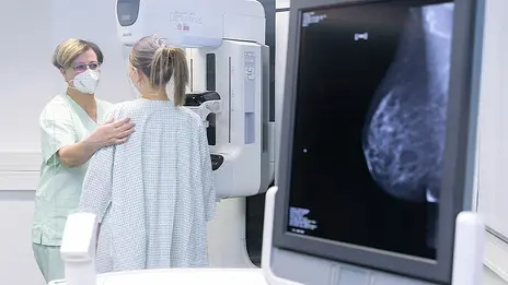 Eine Mitarbeiterin der Radiologie bereitet eine Patientin auf die Mammographie vor. 