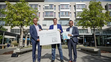 Pressefoto sind Prof. Dr. Achim Jockwig, Vorstandsvorsitzender des Klinikums, Ministerpräsident Dr. Markus Söder und der Staatsminister für Gesundheit und Pflege Klaus Holetschek abgebildet. Sie halten einen Scheck in der Hand. 