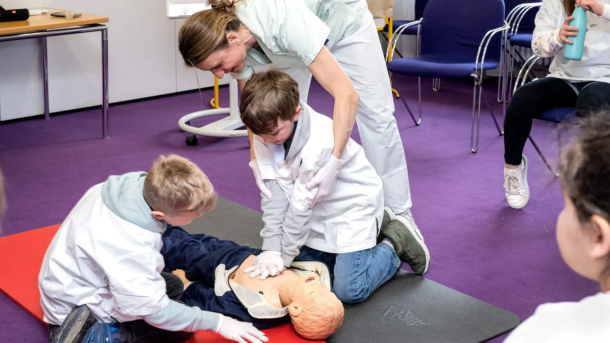 Eine Mitarbeitende des Klinikums leitet zwei Kinder bei der Ersten Hilfe an. 