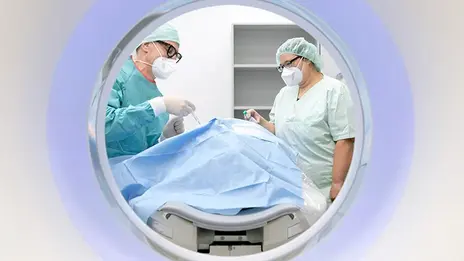 Zwei Mitarbeitende der Neuroradiologie sprechen während der Untersuchung mit einem Patienten. 