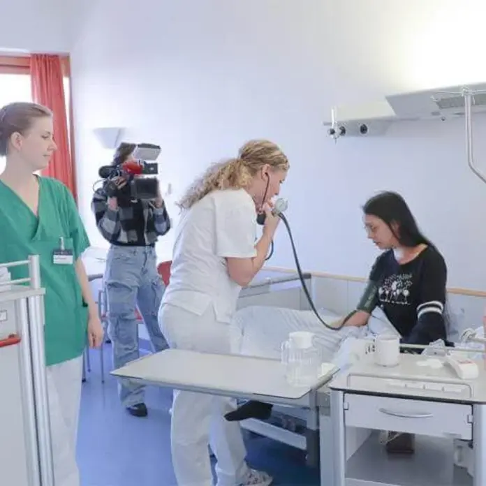 Eine Medizinstudentin und eine Pflegeazubine behandeln eine Patientin. Sie überprüfen die Vitalwerte. 