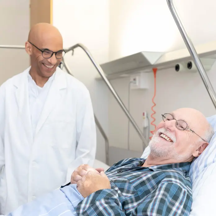 Auf dem Symbolbild spricht ein Arzt mit einem Patienten. Der Mann liegt im Bett. 