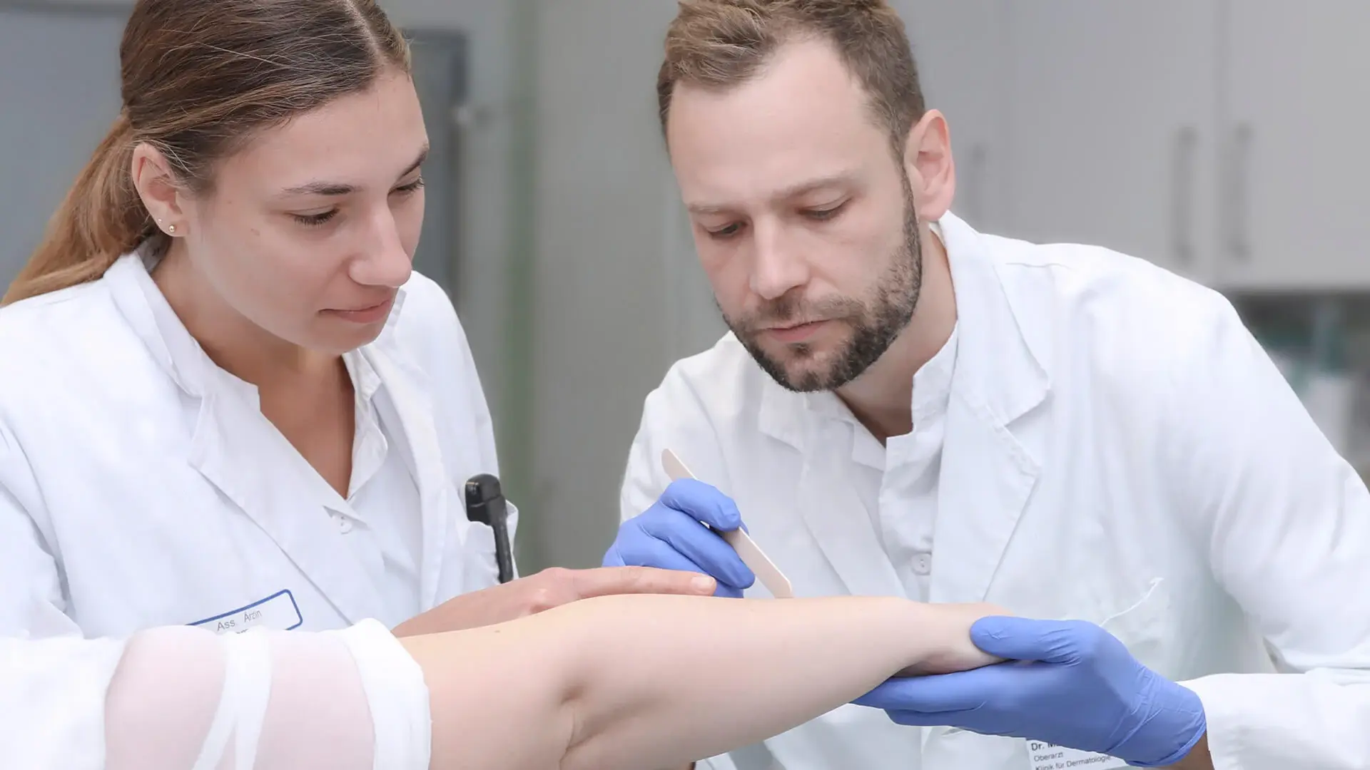 Zwei Mitarbeitende der Hautklinik untersuchen die Haut am Arm einer Patientin. 