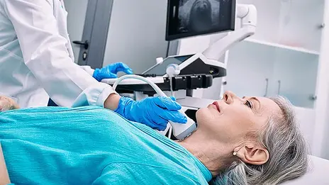 Ein Mitarbeitender führt eine Ultraschalluntersuchung am Hals einer Patientin durch. 