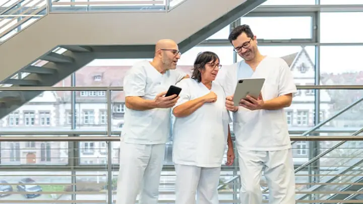 Auf dem Bild sind drei Mitarbeitende des Klinikums zu sehen. Sie halten ein iPad in der Hand und lesen die aktuellen Meldungen zum Thema KIS.