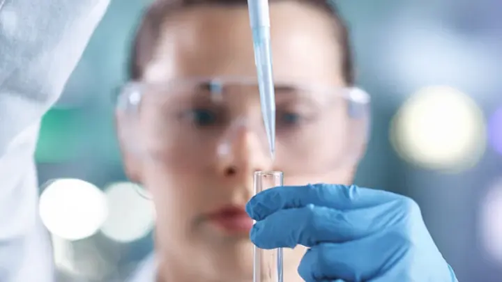 Eine Mitarbeitende füllt mittels Pipette ein Reagenzglas.