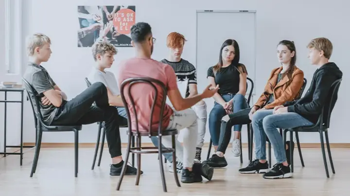 Junge Erwachsene sitzen im Rahmen einer Gruppentherapie zusammen. 