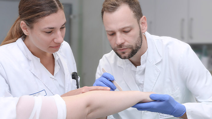 Zwei Mitarbeitende der Hautklinik untersuchen die Haut am Arm einer Patientin. 