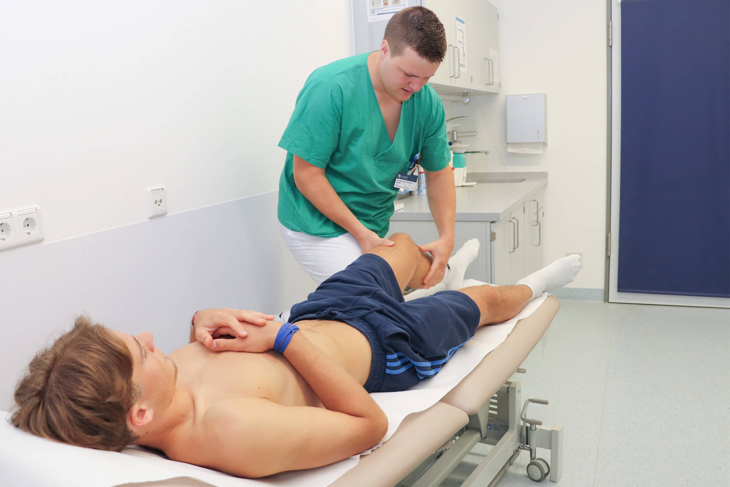 Dr. Johannes Rüther untersucht einen Club-Spieler am Bein. Der Spieler liegt auf einer Liege.